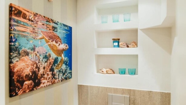 A bathroom with a large painting of a sea turtle, shelves with toiletries, and a light switch. - Cozy 1-room apartment in central Hamburg Altona (Ottensen)