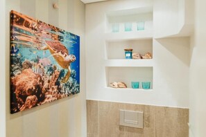 Ein Badezimmer mit einem großen Gemälde einer Meeresschildkröte, Ablagen für Toilettenartikel und einem Lichtschalter.