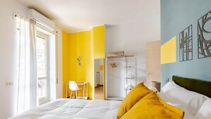 Ett hotellrum med en säng, gula kuddar, ett skrivbord och en stol.