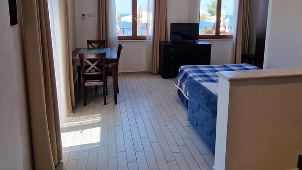 A hotel room with a bed, a TV, a desk with a chair, and large windows with curtains. - Risveglio vista mare 2 (Calafuria)