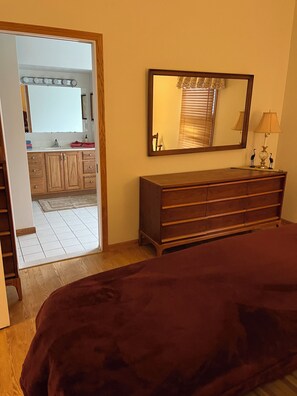 A bedroom with a large bed, a dresser, a mirror, and a view into the bathroom. - Cruising the Huron River Chain of Lakes! 3bed/2.5 bath Lake Front Home (lakeland)