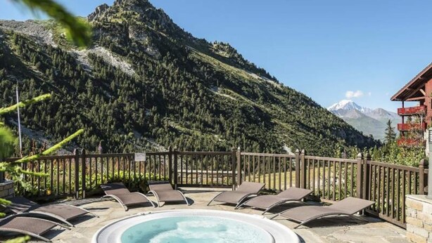 Un bain à remous entouré de chaises longues, avec une vue sur les montagnes en arrière-plan.