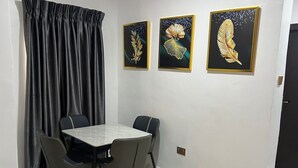 Ein Essbereich mit einem Marmortisch und Stühlen, einem schwarzen Vorhang und drei gerahmten Kunstwerken an der Wand.