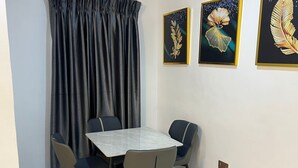 Ein Essbereich mit einem Marmortisch, vier Stühlen, einem dunklen Vorhang und drei gerahmten Kunstwerken an der Wand.
