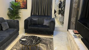 Ein Wohnzimmer mit zwei schwarzen Sofas, einem мраморном журнальном столике, einer großen Pflanze, einem Gemälde und einer Wand mit Spiegeln.