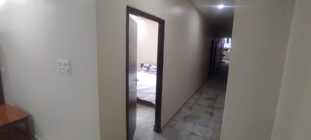 Un pasillo estrecho con una puerta que da a un dormitorio. El pasillo tiene suelo de baldosas y un interruptor de luz en la pared.