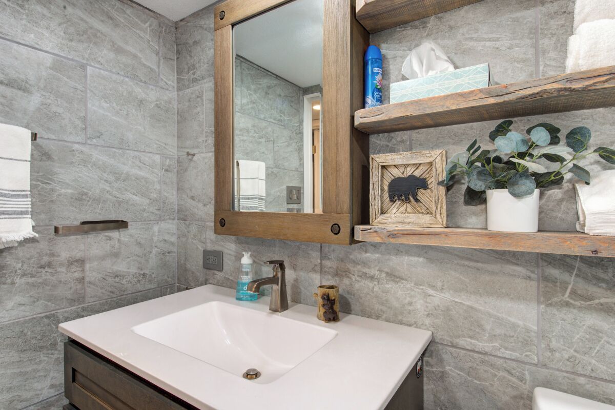 Une salle de bain avec un lavabo blanc, un miroir encadré en bois et une étagère contenant des articles de toilette et un tableau encadré.
