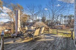 Une terrasse en bois, agrémentée de mobilier d’extérieur, notamment une table et des chaises, entourée d’arbres et d’une clôture.