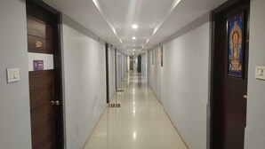 Un largo y estrecho pasillo de hotel con puertas a ambos lados, suelo de baldosas e iluminación empotrada.