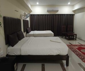 Une chambre d’hôtel avec deux lits, un bureau, une chaise, un climatiseur et un ventilateur.