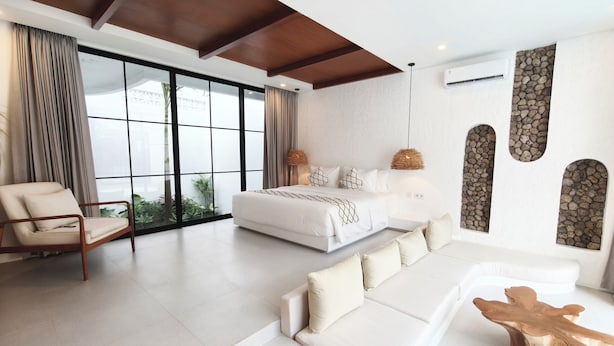 A modern bedroom with a large bed, a sofa, a chair, and a unique wooden coffee table. - Villa Beth Eden Uluwatu  (Ungasan)