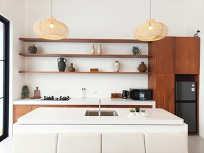 Eine moderne Küche mit weißen Arbeitsflächen, Holzregalen und zwei hängenden Korbtropfenlampen.
