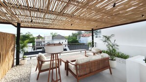 A covered outdoor seating area with wooden furniture and a view of surrounding buildings. - Villa Beth Eden Uluwatu  (Ungasan)