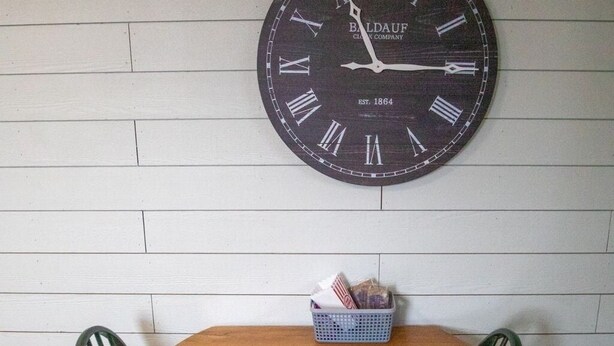 Een eethoek met een houten tafel en twee stoelen, een wandklok en een mand op de tafel.