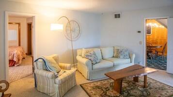 A living room with a sofa, armchair, and a coffee table. There is a lamp and a clock on the wall.