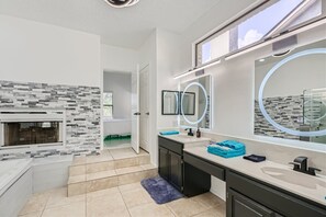 Un baño moderno con salpicadero de piedra, lavamanos dobles y un espejo grande con luz circular.