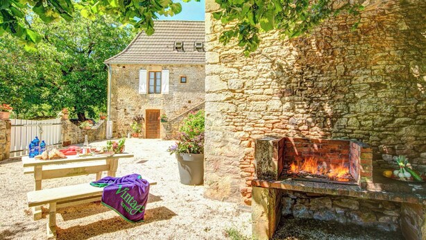 Ein Steinhaus mit Feuerstelle, Picknicktisch und Bank.
