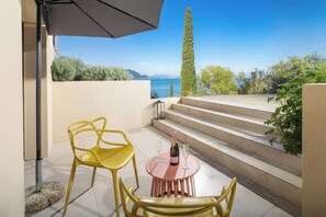 A terrace with yellow chairs, a table, and a bottle of champagne. A staircase leads to a balcony overlooking a body of water and greenery. - Infinity - Four Bedroom Villa, Sleeps 8 (Corfu)