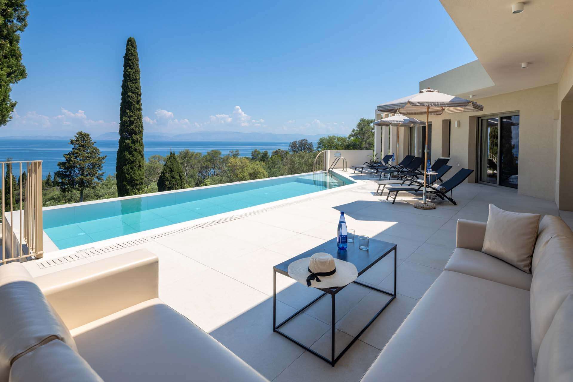 A modern outdoor pool area with a clear view of the sea, lounge chairs, and a sofa.