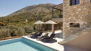 A pool with lounge chairs and umbrellas, a stone building, and a mountainous backdrop. - Kanelo Villa - Three Bedroom Villa, Sleeps 6 (Makryotika)