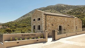 A stone building with a tiled roof, labeled 'Kanelo Villas,' with a mountainous backdrop. - Kanelo Villa - Three Bedroom Villa, Sleeps 6 (Makryotika)
