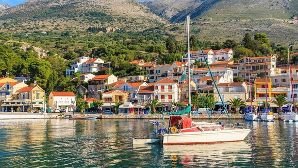 A coastal town with buildings along the waterfront, a boat docked in the foreground, and mountains in the background. - Kanelo Villa - Three Bedroom Villa, Sleeps 6 (Makryotika)