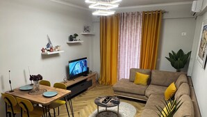 Ett modernt vardagsrum med ett matbord i trä, gula stolar, en soffa med gula kuddar, ett soffbord och en tv.