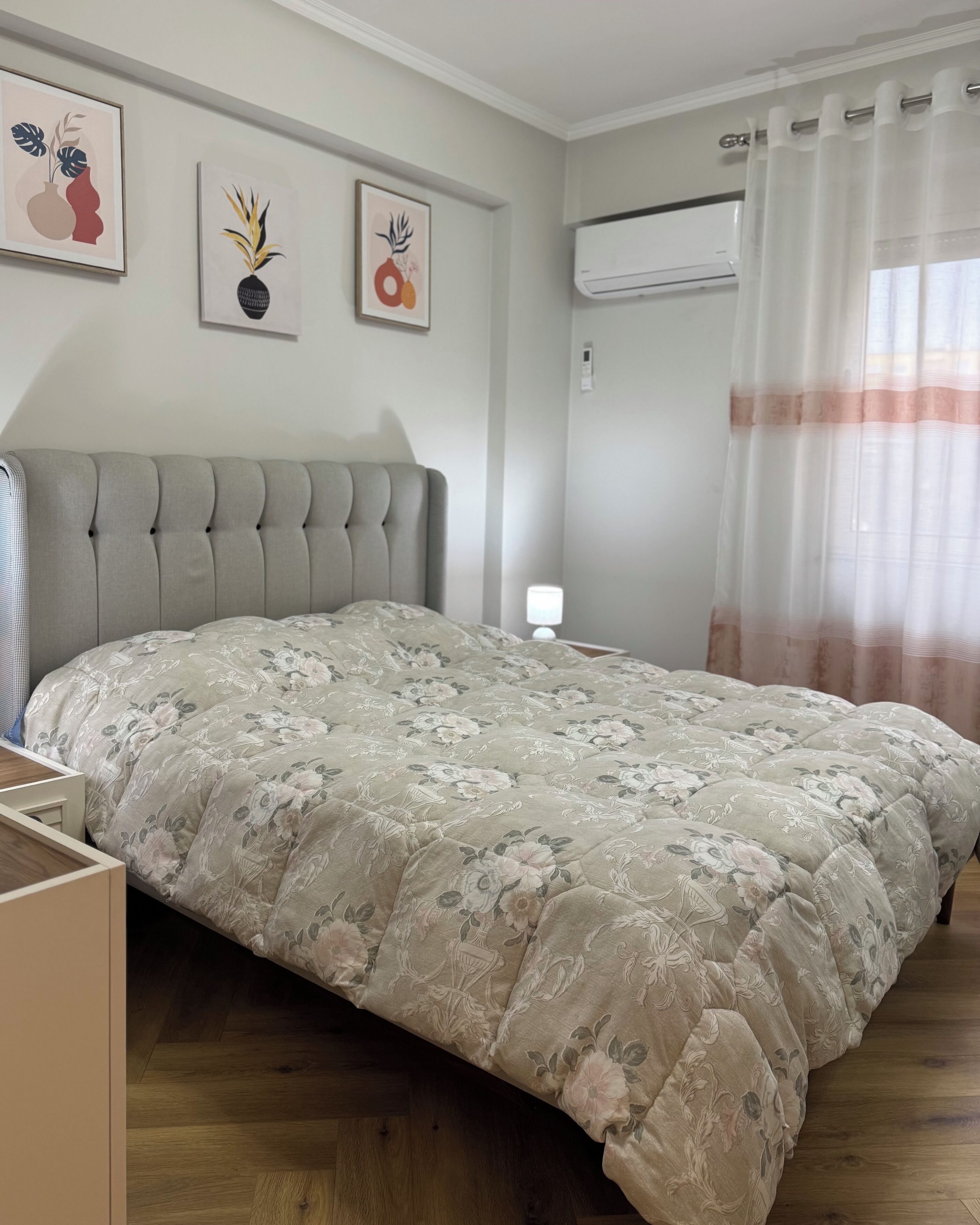 A bedroom with a tufted headboard, floral bedding, and artwork on the wall.
