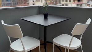 En liten balkong med ett bord och två stolar, med utsikt över en stadssiluett med byggnader och berg.