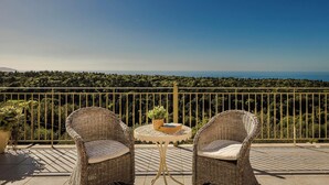 Un balcon agrémenté de fauteuils en osier et d’une petite table, offrant une vue sur un paysage luxuriant et la mer.
