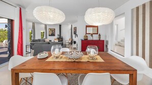 Een moderne eetruimte met een houten tafel, witte stoelen en twee grote hanglampen.