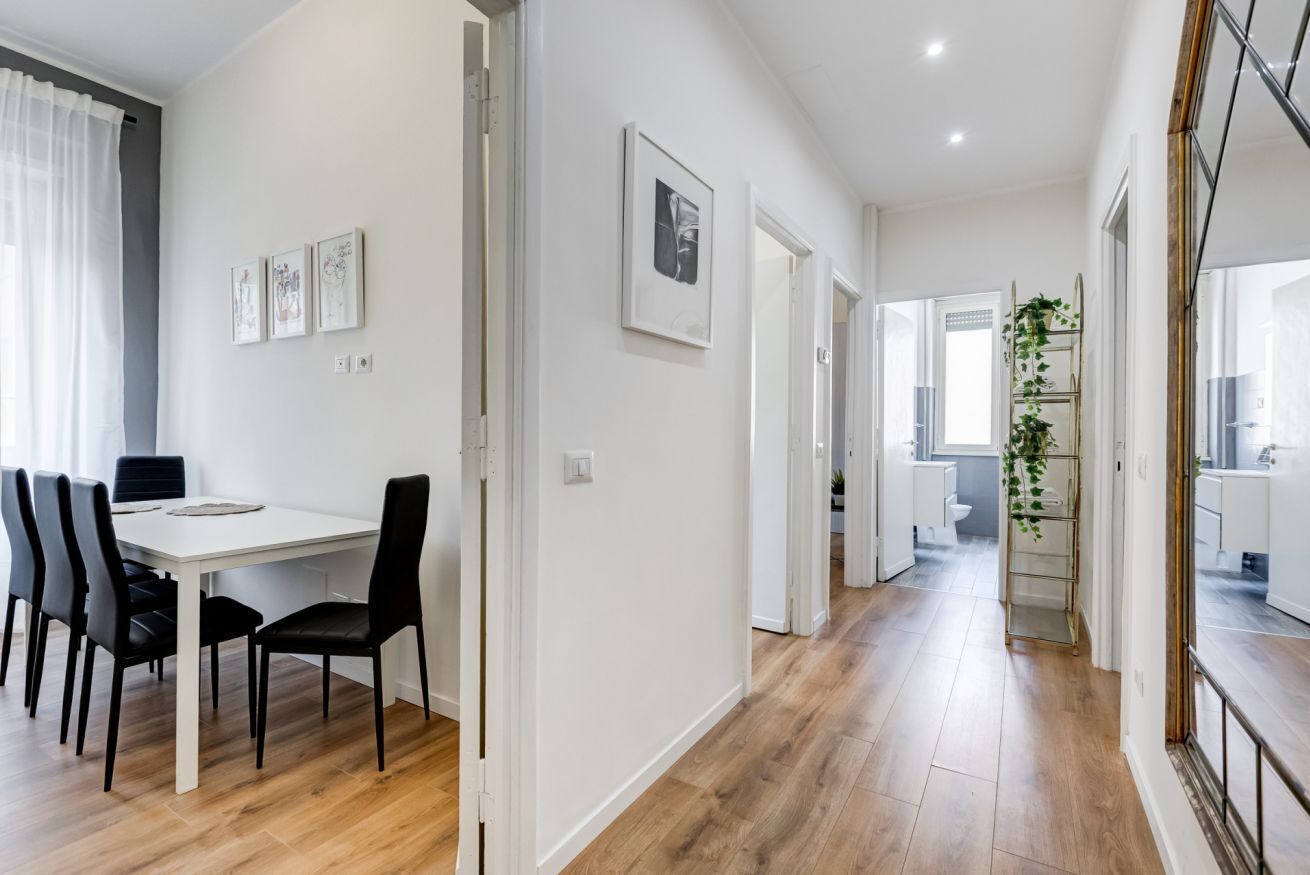 A modern interior with a dining area, a hallway leading to a bathroom, and a staircase.