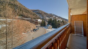 A mountain view from a balcony with a wooden railing, overlooking a road with parked cars and buildings in the valley. - C. du Verdon Ndeg3307 - 2P6 (Allos)