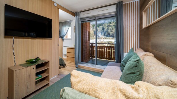 A modern room with a wooden wall, a flat-screen TV, a sofa, a small table, and a sliding glass door leading to a balcony. - C. du Verdon Ndeg3307 - 2P6 (Allos)