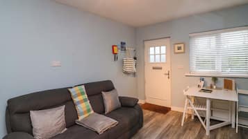 Una sala de estar con un sofá marrón oscuro, un escritorio blanco y una puerta con ventanal.
