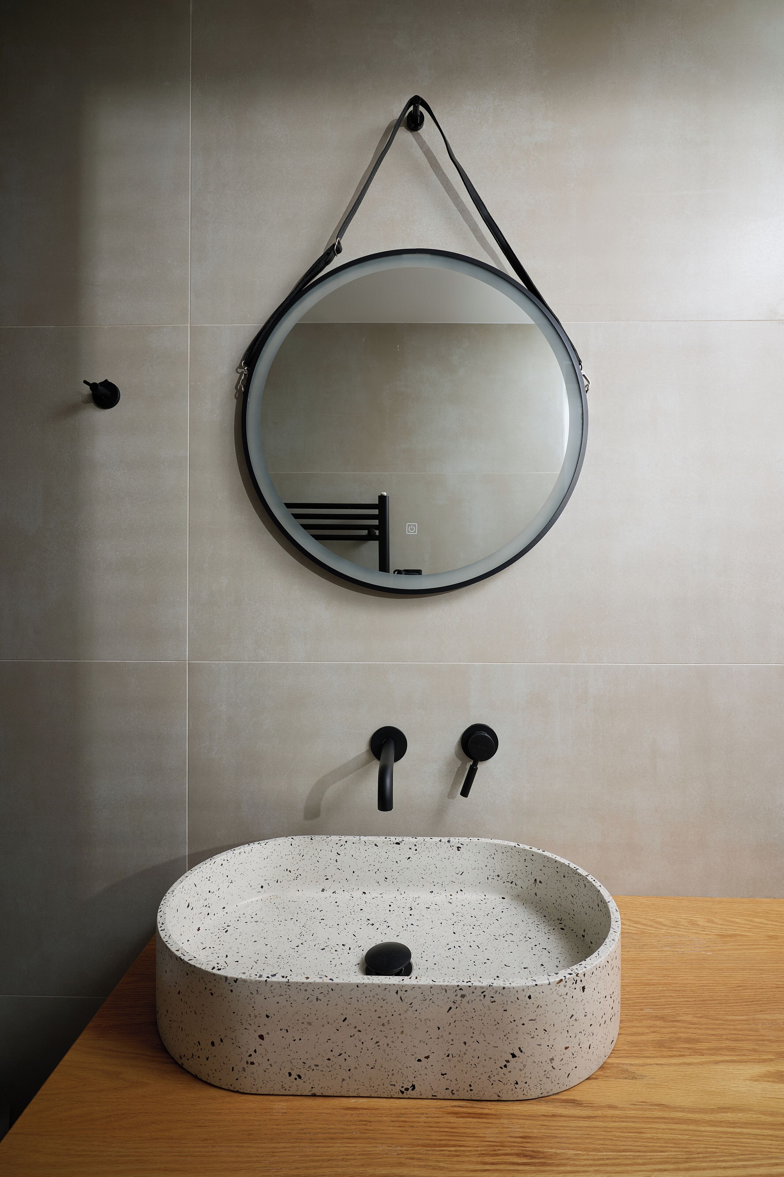 Un baño moderno con un lavabo redondo y con motas, un espejo montado en la pared y un perchero para toallas.
