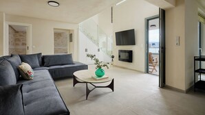 A modern living room with a grey sectional sofa, a round coffee table with a green vase, and a staircase leading to another level. - up to 20 pax Myrtia Villa & Cave Estate with Pool & Hot tub by Chic Greek Villas (Myrtia)