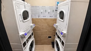 A laundry room with two stacked washing machines, a tiled wall with informational posters, and a drain in the floor. - Miami Beach Charm Inviting 1br Space (Miami Beach)