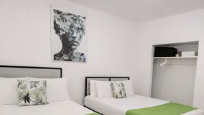A room with two beds, each with a green throw blanket and white bedding. There is a black and white artwork on the wall above the beds. - Miami Beach Charm Inviting 1br Space (Miami Beach)