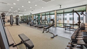 Un gimnasio con diverso equipo de ejercicio, amplias ventanas y un ventilador de techo.