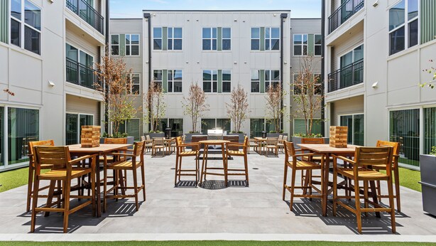Un patio con mobiliario exterior, una chimenea en el centro y un edificio con varios balcones.