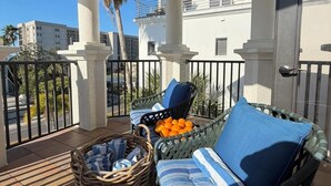 Ein Balkon mit Korbmöbeln, einer Orangenschale und Blick auf Palmen und Gebäude.