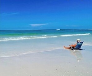 A person sitting on a beach chair facing the ocean, with waves approaching the shore. - Last Minute Availability Siesta Key Dream 100 ft to Beach  Walk Everywhere  (Siesta Key)