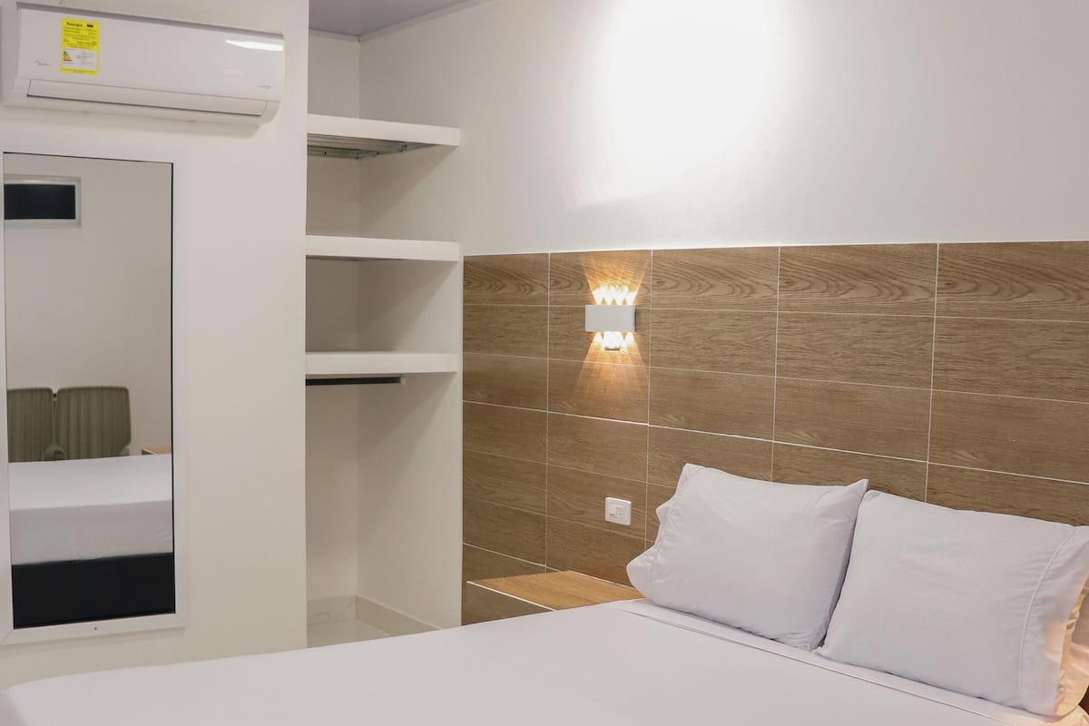 Une chambre d’hôtel comprenant un lit, une table de chevet, une lampe fixée au mur et une étagère intégrée.