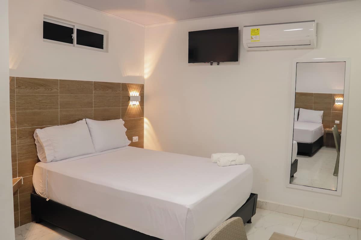 Une chambre d’hôtel équipée d’un lit, d’un téléviseur fixé au mur, d’un appareil de climatisation et d’un miroir.