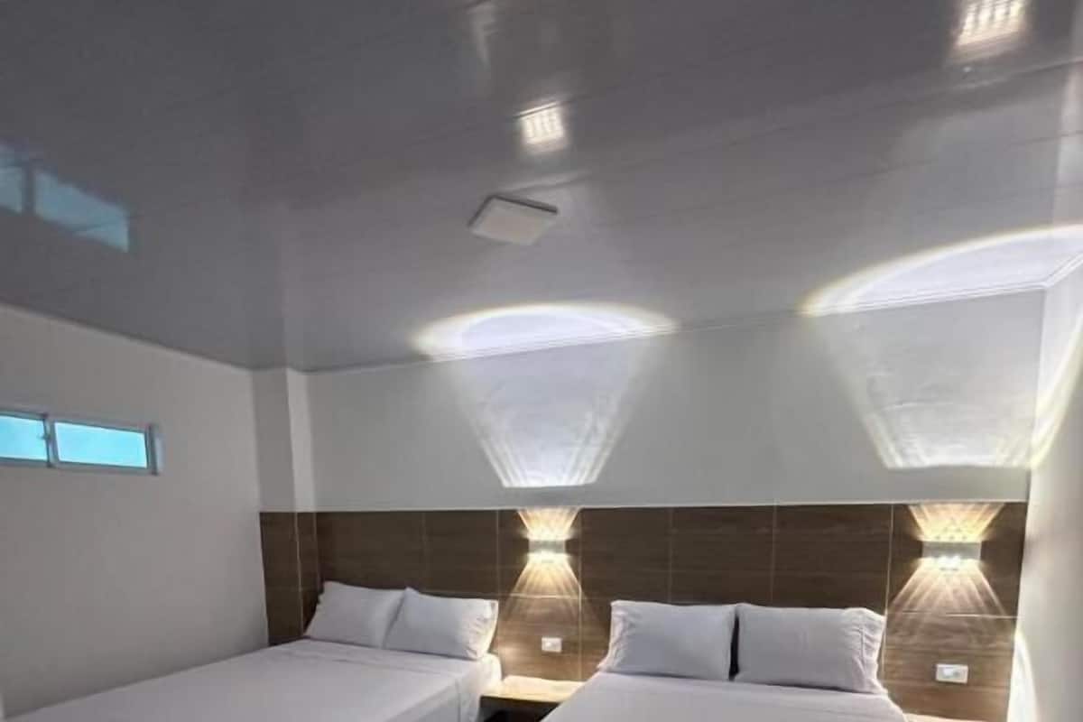 Une chambre d’hôtel avec deux lits simples, une petite fenêtre et un luminaire fixé au mur.