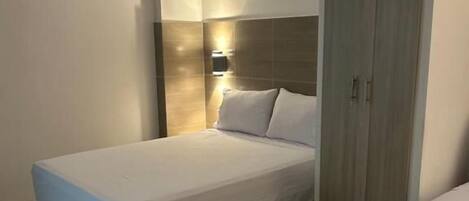 Une chambre d’hôtel équipée d’un lit, d’une armoire et d’un luminaire fixé au mur.