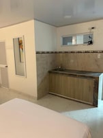 Una habitación de hotel con una cama, una kitchenette pequeña con un lavamanos y un espejo sobre la encimera.