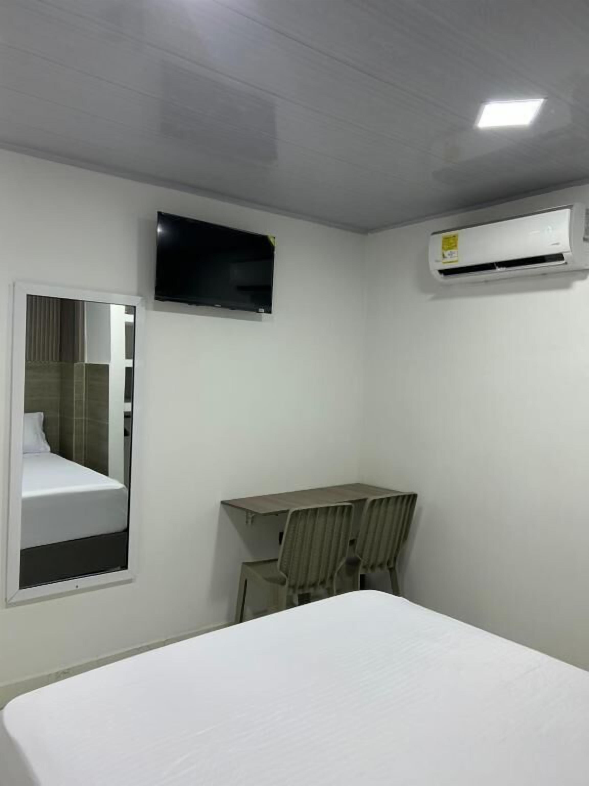 A hotel room with a bed, a desk, a chair, a flat-screen TV, and an air conditioning unit.