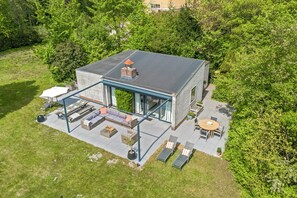 A modern house with a patio, outdoor seating, and a large window overlooking a garden.